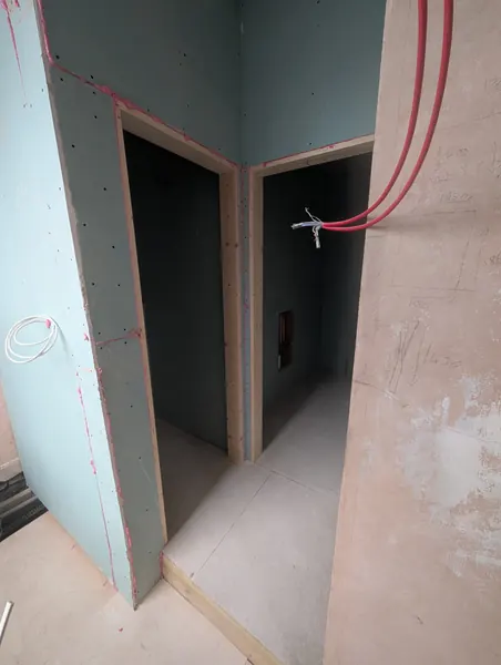 Boarded stud partitions forming two door openings, with red pipework above