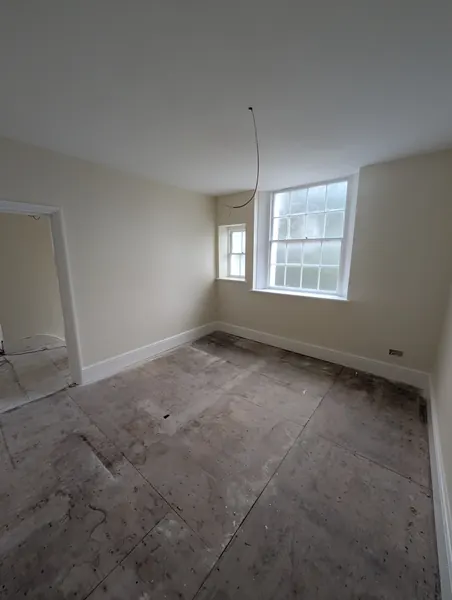 The freshly painted room with a sash window, white skirting and a doorway on the left