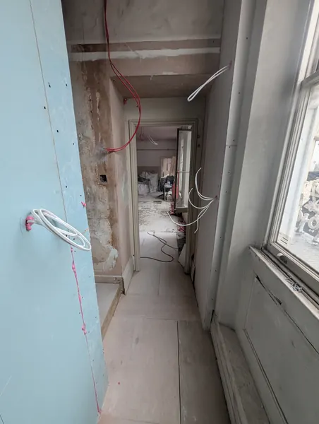 A long corridor of new boarded partitions with loose cabling and a sash window on the right
