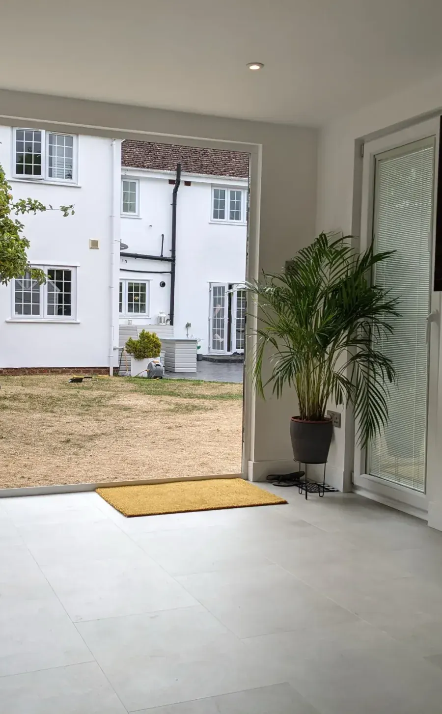 Looking out from inside a garden room through open bifold doors onto a lawn and house beyond