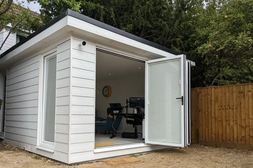 White composite garden office with bifold doors open onto the lawn, desk and chair inside