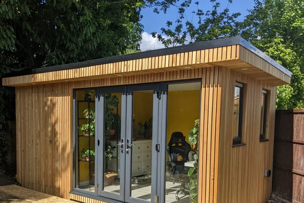 Cedar-clad garden room with full-height bifold doors under a blue sky