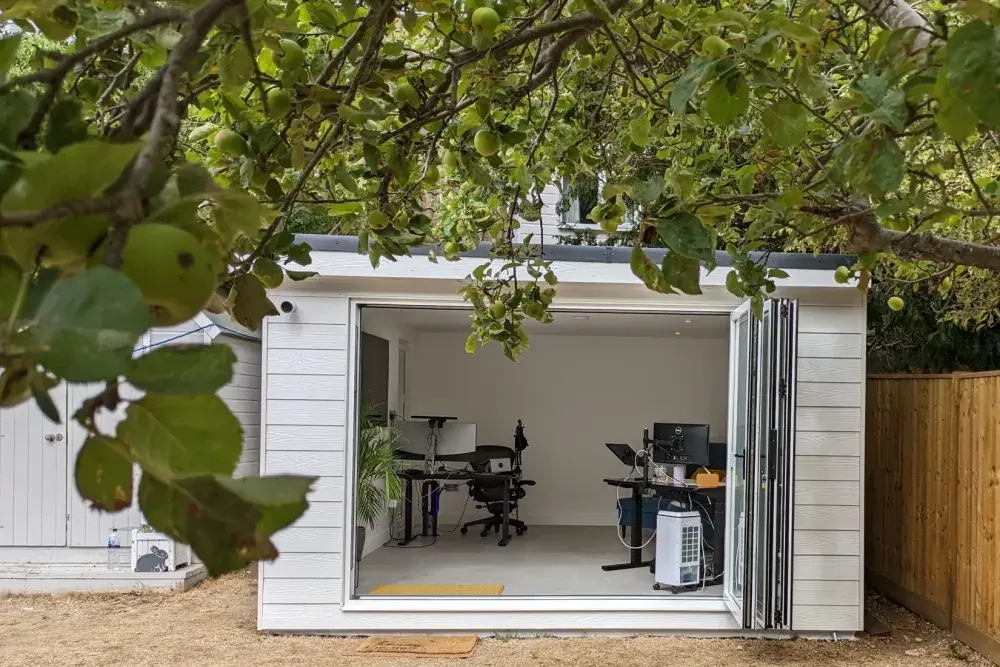 Garden office seen through the branches of an apple tree, bifold doors folded back