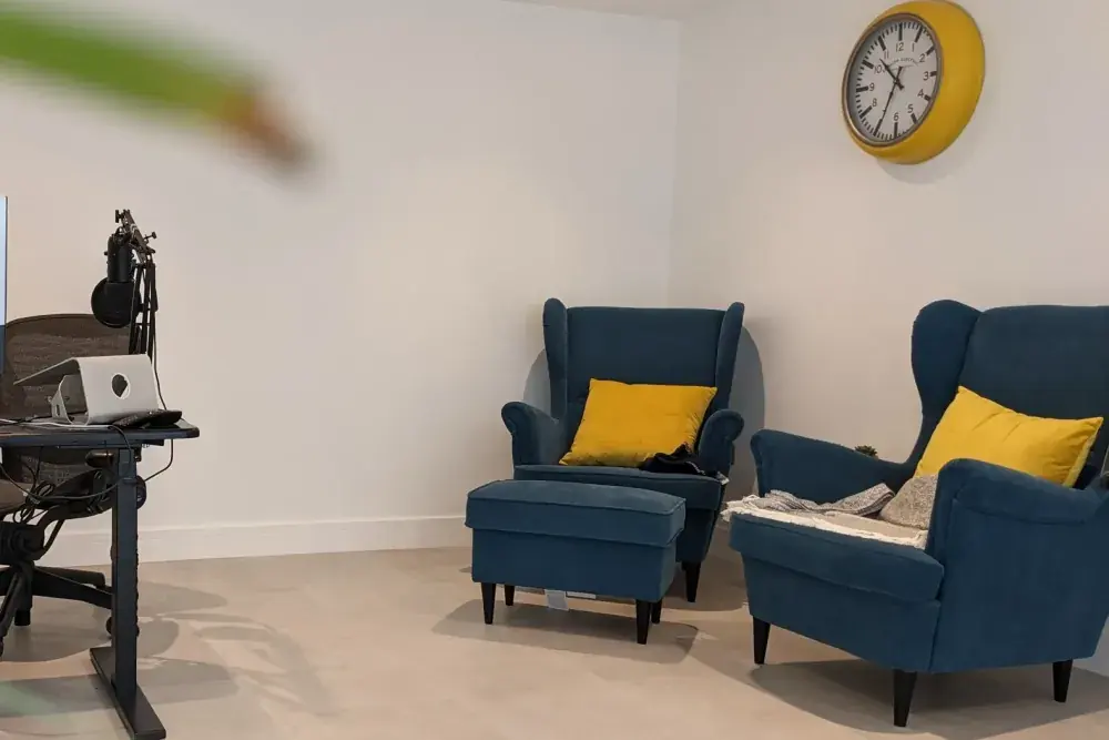 Garden room interior with two teal armchairs, yellow cushions and a wall clock