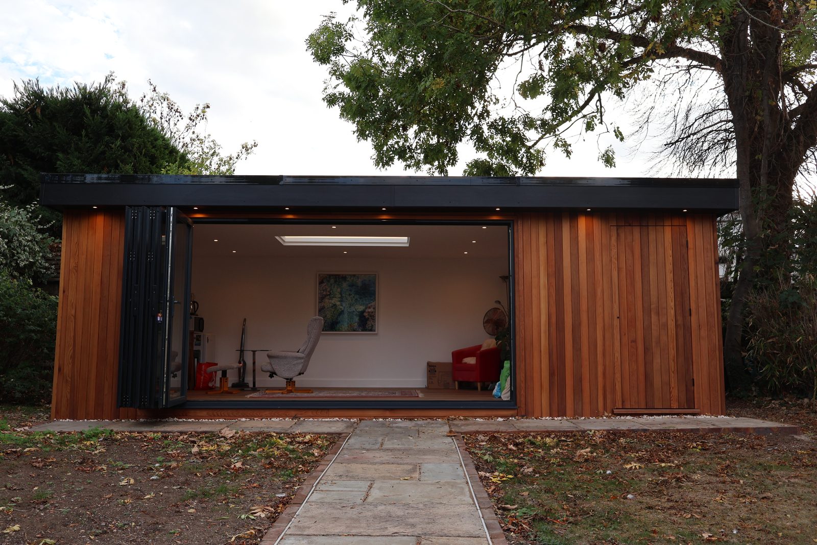 The garden office with its bi-fold doors folded back, showing a bright room with a roof light, at the end of a paved path